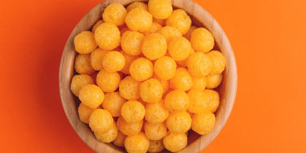 Cheese puff balls in wooden bowl on bright colorful background